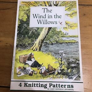 以下が含まれることがあります： 「The Wind in the Willows」のイラストが描かれた本の表紙。緑と黄色の背景にピクニックのシーンが描かれています。タイトルは白いボックスに入っています。表紙の下部には、Gary Kennedyによる「4 Knitting Patterns」と書かれています。