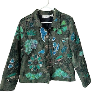 May include: A green jacket with a distinctive design. The jacket has a dark green base with appliqued shapes in shades of green and blue. It features a button-up front and long sleeves. The jacket is displayed on a white hanger.