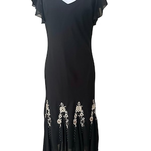 May include: Black formal dress with a V-neckline and flutter sleeves. The dress features an embroidered floral design in cream and gold along the hemline. The skirt has a flared, asymmetrical hem.
