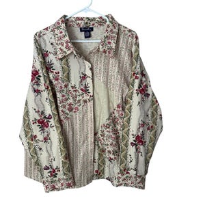 May include: A long-sleeve button-down shirt featuring a patchwork design with cream, red, and green floral patterns, vertical stripes, and eyelet lace panels. The shirt has a pointed collar and a label reading Den & Co. at the inner neckline.