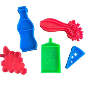 May include: A collection of colorful plastic food-shaped toys. Includes a blue soda bottle, red grapes, a red celery stalk, a green milk carton with the word "Milk", and a blue pizza slice with the text "CH-383".