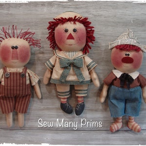 May include: Three handmade rag dolls with red hair. The doll on the left is wearing overalls, the middle doll is wearing a sailor outfit, and the doll on the right is wearing a newspaper hat and overalls. The dolls are standing on a wooden background with the text "Sew Many Prims".