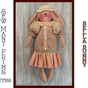 Könnte beinhalten: Eine handgefertigte Stoffpuppe mit einem braunen und rosafarbenen Kleid, einem rosafarbenen Hut und einem braunen Gesicht. Die Puppe steht auf einer Holzoberfläche. Der Text "SEW MANY PRIMS PATTERNS" befindet sich auf der linken Seite des Bildes und "BELLA BUNNY" auf der rechten Seite des Bildes.