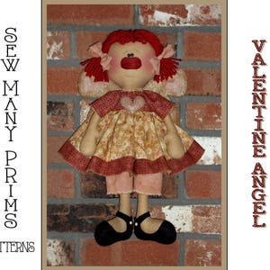 May include: A handmade Valentine's Day angel doll with red hair, a red heart on her dress, and a brick background. The doll is wearing a brown and red dress with a white and pink gingham skirt.  The doll is holding a red heart in her hands.  The text "Valentine Angel" is printed on the right side of the image.  The text "Sew Many Prims Patterns" is printed on the left side of the image.