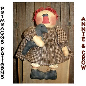 May include: A handmade rag doll with red hair and a black and white checkered dress. The doll is holding a black bird in its arms. The doll is standing on a wooden surface. The text "Annie & Crow" is visible in the background.