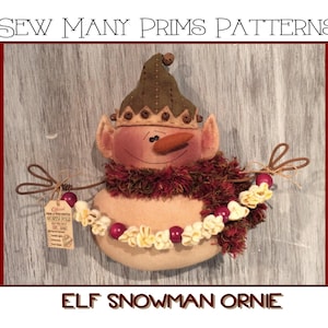 May include: A handmade elf snowman ornament with a green hat, brown fur trim, and a red and white popcorn garland. The ornament has a tag that says "From a True Santa's North Pole Workshop".