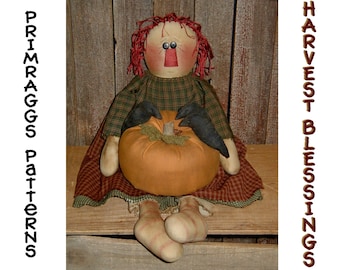 May include: A handmade rag doll with red hair and a plaid dress holds a small orange pumpkin. The doll is sitting on a wooden bench with the words "HARVEST BLESSINGS" and "PRIMRAGGS PATTERNS" on either side.