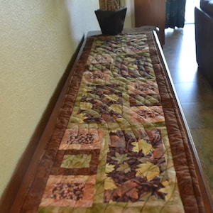 Fall table runner with beautiful leaf fabric patterns in geometric layout with machine quilted pattern.  13.5 x 50.5 long.  made in USA