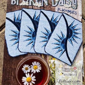 May include: A set of four blue and white fabric placemats with a daisy design. The placemats are titled "Broken Daisy Placemats" and are from the company "Timeless Treasures Wildflowers Quiltworx.com". The placemats are made using foundation paper piecing.