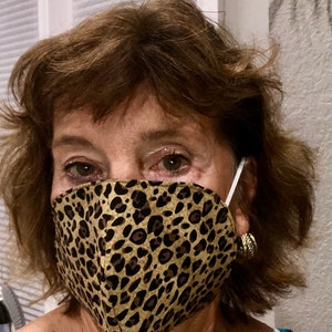 May include: A woman wearing a brown and black leopard print face mask. The mask has a white elastic strap.