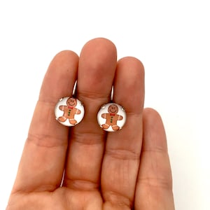 May include: A pair of gingerbread man earrings with white backgrounds and silver settings.
