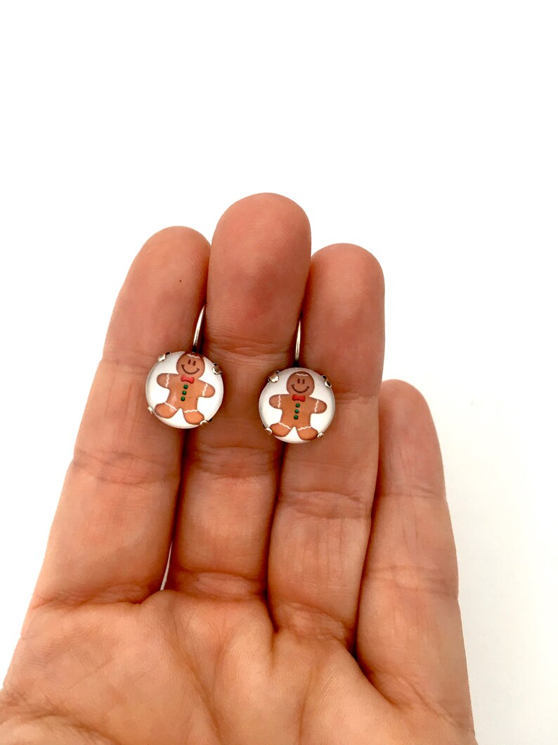 May include: A pair of gingerbread man earrings with white backgrounds and silver settings.