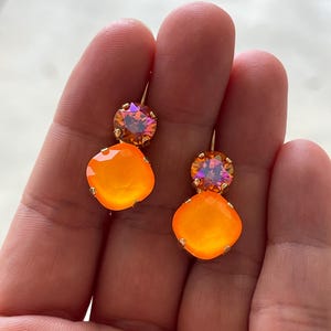 Può includere: Un paio di orecchini pendenti con due pietre di cristallo arancioni e iridescenti su ogni orecchino.