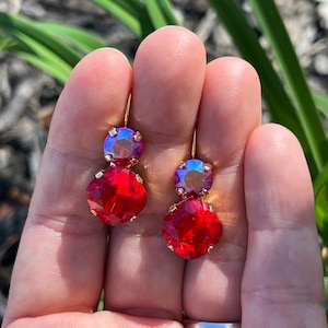 May include: A pair of gold earrings with red and iridescent purple crystal stones. The earrings are dangling and have a simple design.