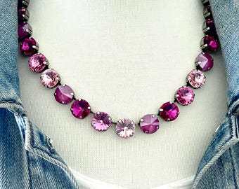 May include: A necklace featuring a series of round, faceted crystals in varying shades of pink and magenta, set in dark metal prongs. The crystals are arranged in a single strand, creating a gradient effect from light to dark pink.