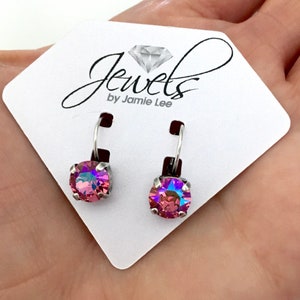 May include: A pair of silver dangle earrings with pink iridescent crystal stones. The earrings are on a white card with the text "Jewels by Jamie Lee".
