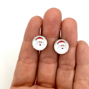 May include: A pair of silver hoop earrings with a white round charm featuring a cartoon image of Santa Claus with a red hat.