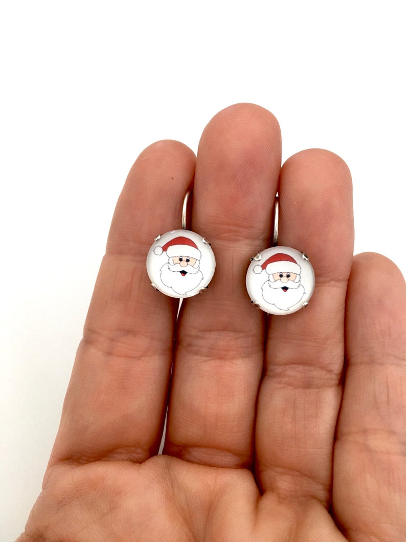 May include: A pair of silver hoop earrings with a white round charm featuring a cartoon image of Santa Claus with a red hat.