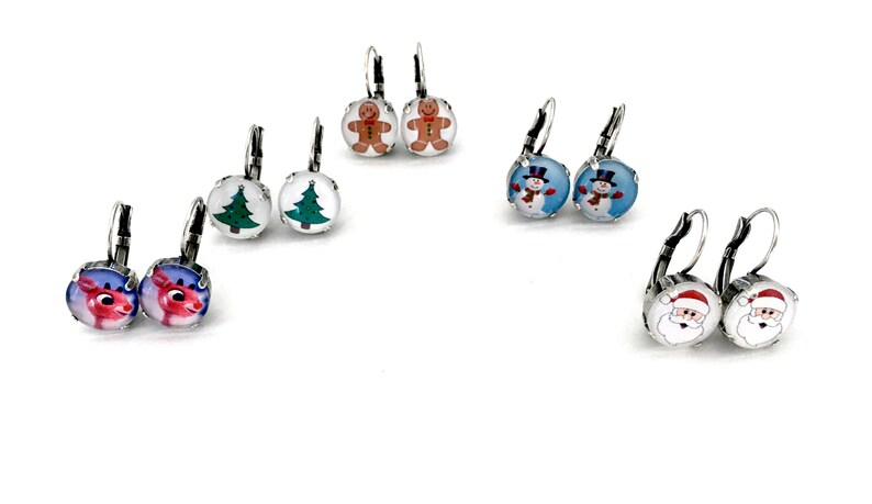May include: Assortment of Christmas themed earrings with various designs including a snowman, Santa Claus, a gingerbread man, a Christmas tree, and a reindeer. The earrings are silver with a round glass charm.