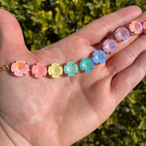 Peut inclure: Un arc-en-ciel de perles de verre iris&eacute;es avec des montures dor&eacute;es. Les perles sont dispos&eacute;es en ligne sur une main, en commen&ccedil;ant par le rose et en terminant par le bleu.