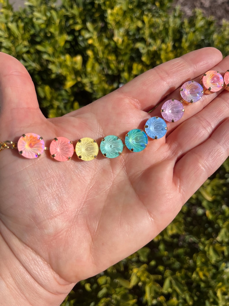 Peut inclure: Un arc-en-ciel de perles de verre iris&eacute;es avec des montures dor&eacute;es. Les perles sont dispos&eacute;es en ligne sur une main, en commen&ccedil;ant par le rose et en terminant par le bleu.