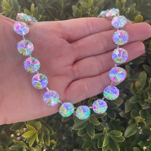 May include: A silver necklace with iridescent round stones. The necklace is made of a chain with round stones attached to it. The stones are iridescent and have a rainbow effect.