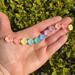 Peut inclure: Un arc-en-ciel de perles de verre iris&eacute;es avec des montures dor&eacute;es. Les perles sont dispos&eacute;es en ligne, les couleurs passant du rose au jaune, puis au vert et au bleu.