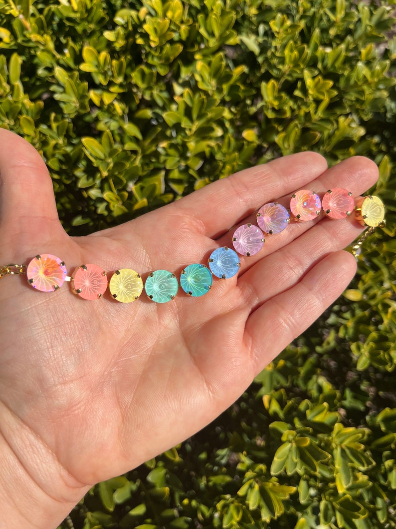 Peut inclure: Un arc-en-ciel de perles de verre iris&eacute;es avec des montures dor&eacute;es. Les perles sont dispos&eacute;es en ligne, les couleurs passant du rose au jaune, puis au vert et au bleu.