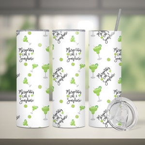 May include: White insulated tumbler with a repeating pattern of green margarita glasses and lime slices. The text "Margaritas, Lime & Sunshine" is displayed in black script. Includes a silver straw and lid.
