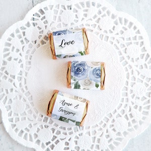 Puede incluir: Tres pequeñas barras de chocolate con diseños florales de rosas azules y grises y las palabras "Love" y "Azure & Grayson" en los envoltorios. Las barras están dispuestas sobre un mantel individual de papel blanco y encaje.