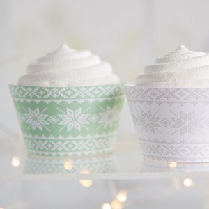 Könnte beinhalten: Zwei weiße, mit Zuckerguss überzogene Cupcakes mit grünen und weißen gemusterten Cupcake-Förmchen. Die Förmchen haben ein Schneeflockenmuster.