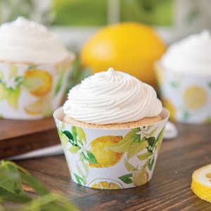 May include: Three white cupcakes with lemon-themed wrappers. The cupcakes have white frosting and are arranged on a wooden surface.
