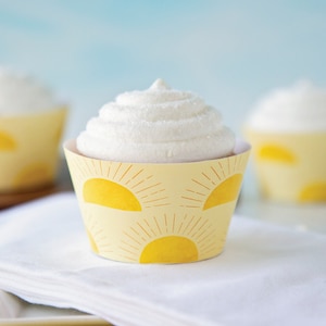 May include: Yellow cupcake liners with a sunburst pattern. The liners are decorated with yellow suns and white rays. The cupcakes are topped with white frosting.