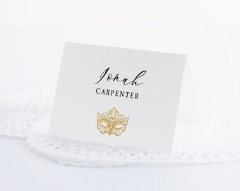 May include: White place card with black calligraphy that reads "Jonah Carpenter" and a gold glitter masquerade mask.