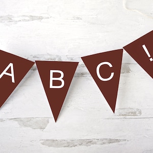 May include: A brown paper banner with white letters spelling out "ABC!" hanging on a white wooden background.