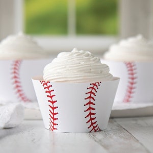 May include: Three white cupcakes with white frosting, decorated with red baseball stitching on the cupcake liners.
