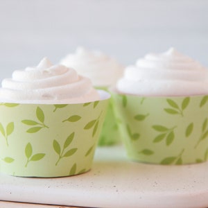 May include: Three white frosted cupcakes with green leaf patterned cupcake liners.