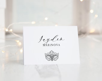 May include: A white card with black text that reads "Jayden Marinova" and a black and white illustration of a masquerade mask.