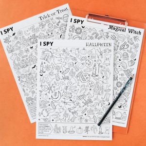 May include: Three black and white Halloween-themed "I Spy" activity sheets with various illustrations, including pumpkins, ghosts, and witches. The sheets are held together by a clear clipboard, with a pencil resting on top. The words "Trick-or-Treat", "Halloween", and "Magical Witch" are visible.