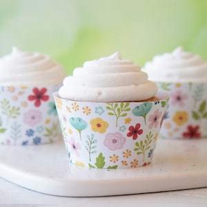 May include: Three cupcakes with white frosting and floral patterned cupcake liners. The liners have a white background with colorful flowers and leaves.