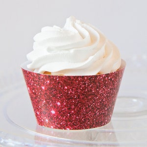 May include: A cupcake with white frosting in a red glitter cupcake liner. The cupcake is on a clear glass plate. The red liner has a glittery texture.
