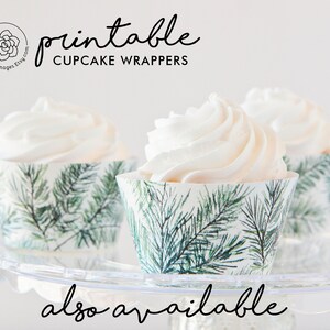 May include: Three cupcakes with white frosting in decorative cupcake wrappers. The wrappers have a green and white pine needle design. The text "printable CUPCAKE WRAPPERS" is displayed above the cupcakes.