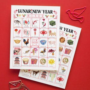 May include: Two Lunar New Year Bingo cards with colorful illustrations of cultural symbols, including lanterns, lucky knots, and dumplings. The cards are on a red background, with the text "LUNAR NEW YEAR" at the top.