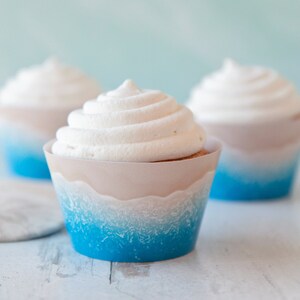 May include: Three cupcakes with white frosting and blue and white ombre cupcake liners. The liners have a wave design.