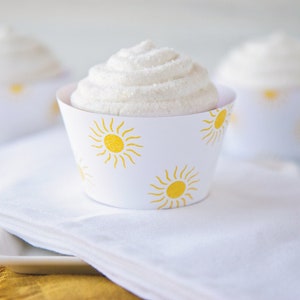 May include: White cupcakes with white frosting and yellow sun designs on the cupcake liners.