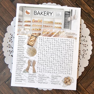 以下が含まれることがあります： BAKERY WORD SEARCHと題された印刷済みのアクティビティシート。パンが並ぶベーカリーの内部の線画、探すべき焼き菓子のリスト、文字のグリッド、そしてパンの小さなイラストが描かれています。