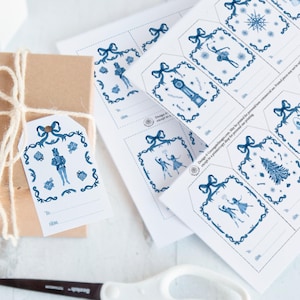 May include: A set of printable gift tags featuring a blue and white snowflake, a clock, a nutcracker, a ballerina, and a Christmas tree. The tags have a space for writing "To:" and "From:".