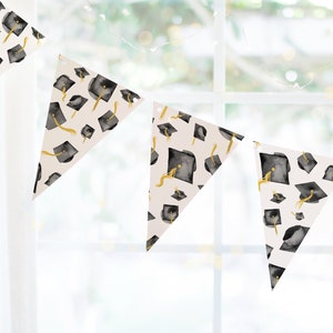 Puede incluir: Una pancarta de fiesta de graduación con fondo blanco y gorros de graduación negros y dorados. La pancarta está hecha de banderas triangulares.