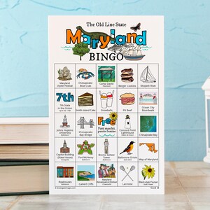 Puede incluir: Una tarjeta de Bingo de Maryland con ilustraciones coloridas de monumentos e iconos de Maryland, incluyendo un dinosaurio, un velero y un cangrejo. La tarjeta incluye el texto "The Old Line State" y "Maryland BINGO".