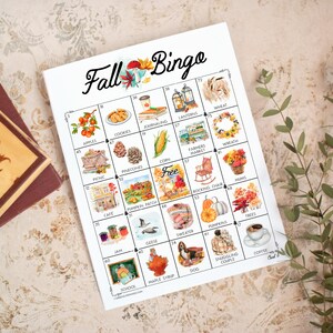 Peut inclure: Une carte de jeu Fall Bingo en papier blanc présentant une grille de vingt-cinq cases avec des illustrations aquarelles colorées d'éléments sur le thème de l'automne comme des pommes, des citrouilles, des pommes de pin et un pull.